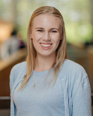 Kayla has blonde hair and blue eyes. She is smiling and wearing a blue shirt